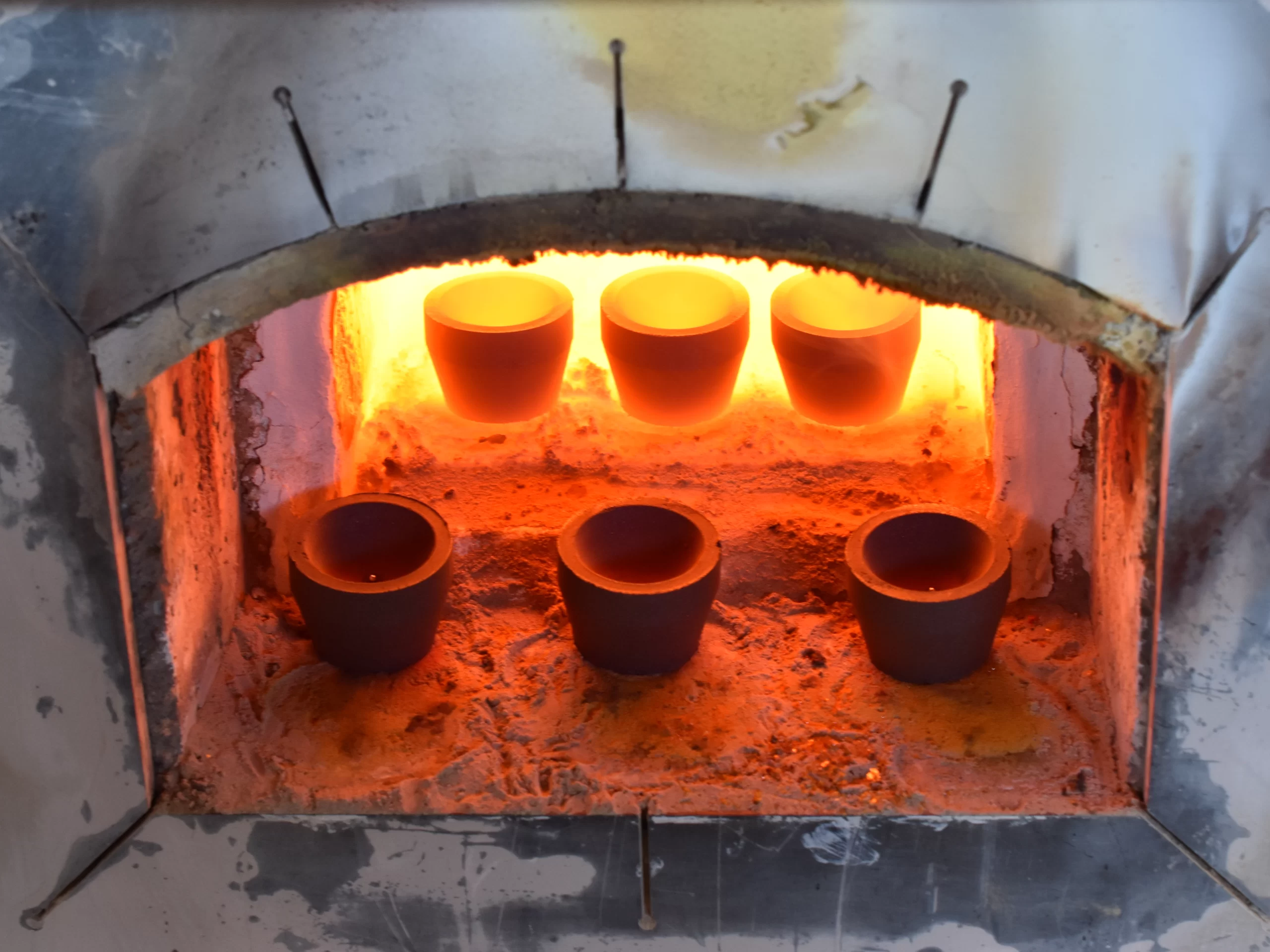 Three glowing crucibles in a hot furnace chamber for fire assay